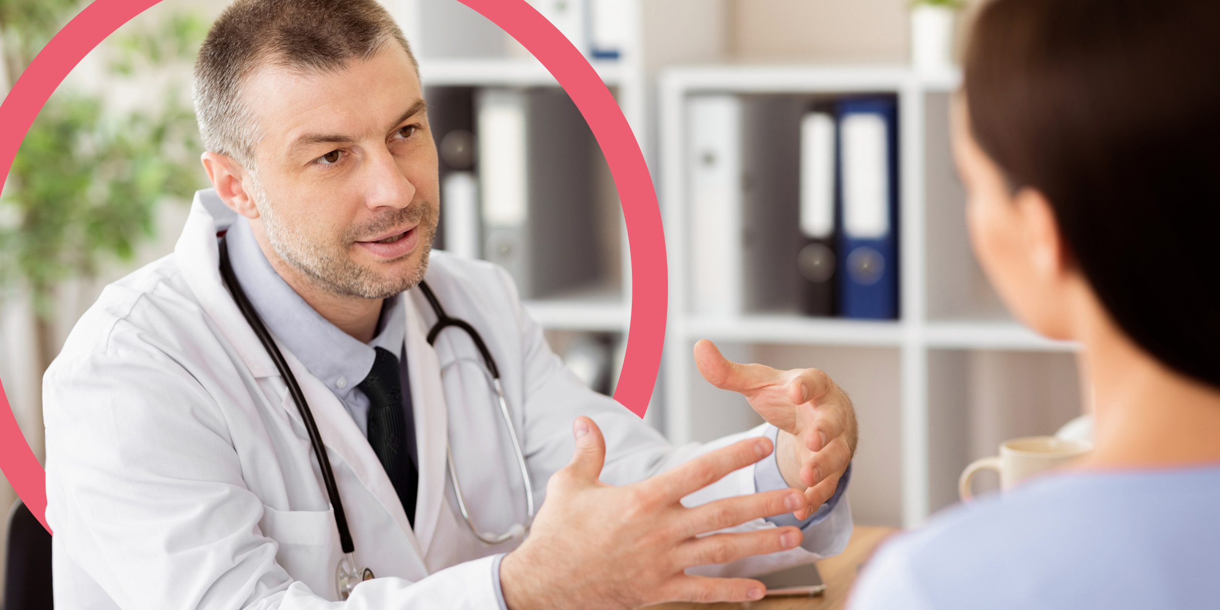 Arzt sitzt einer Patientin gegenüber, erklärt ihr etwas und gestikuliert dabei mit den Händen. Hinter ihm zeigt sich ein pinker Ring als Designelement.