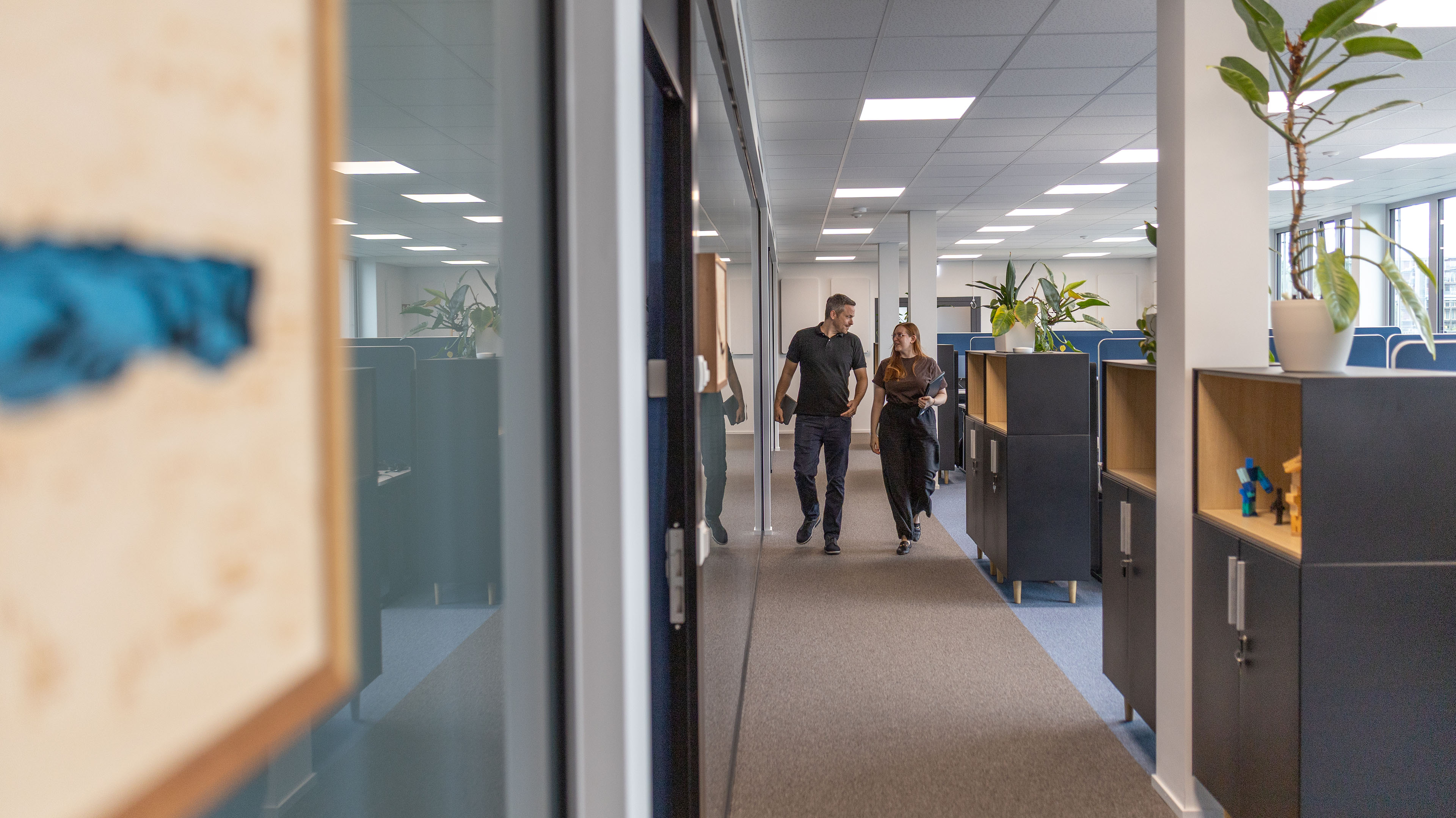 Two employees walk down the office corridor and talk.