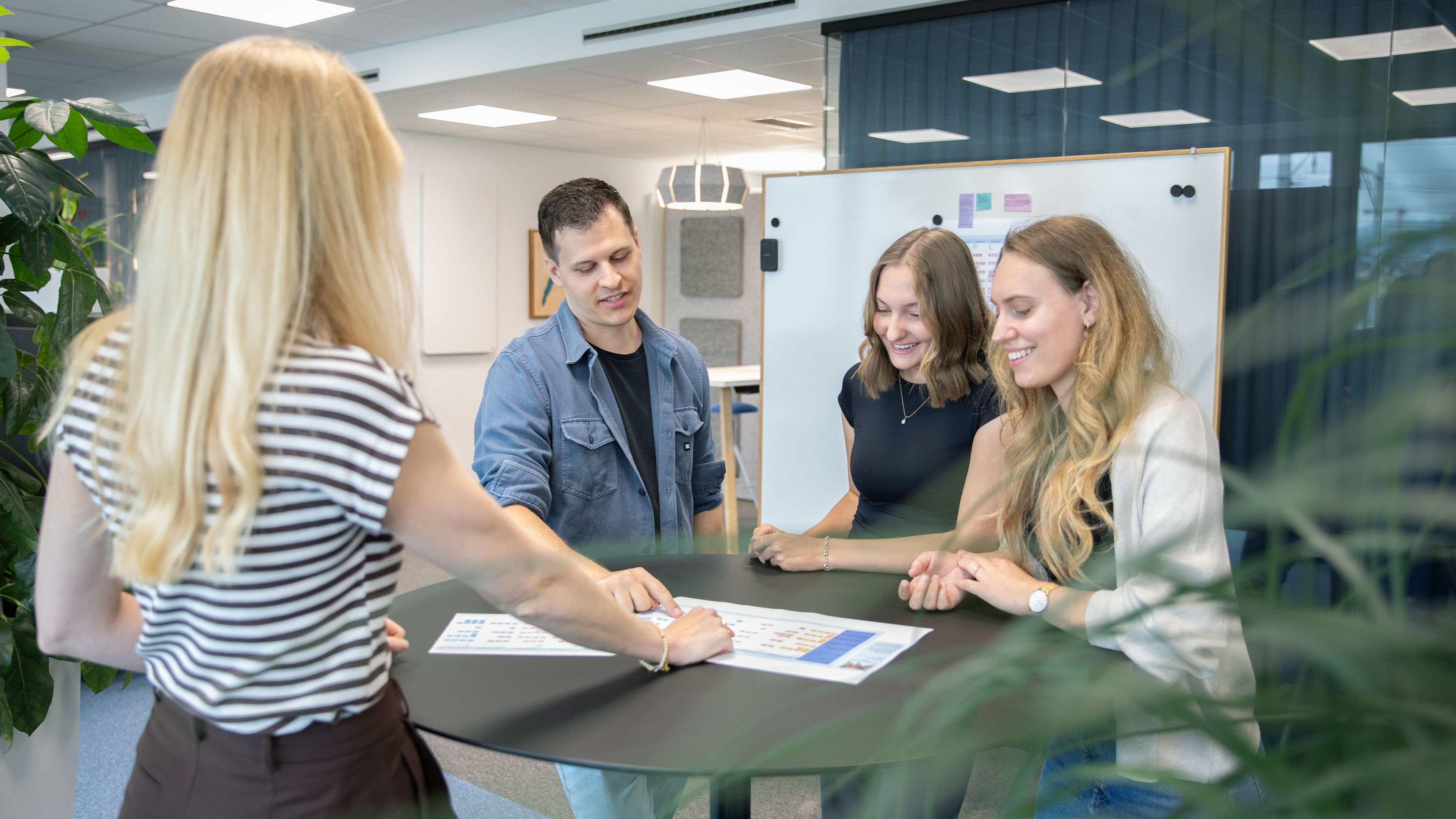 Four employees stand at a table and discuss a document together.