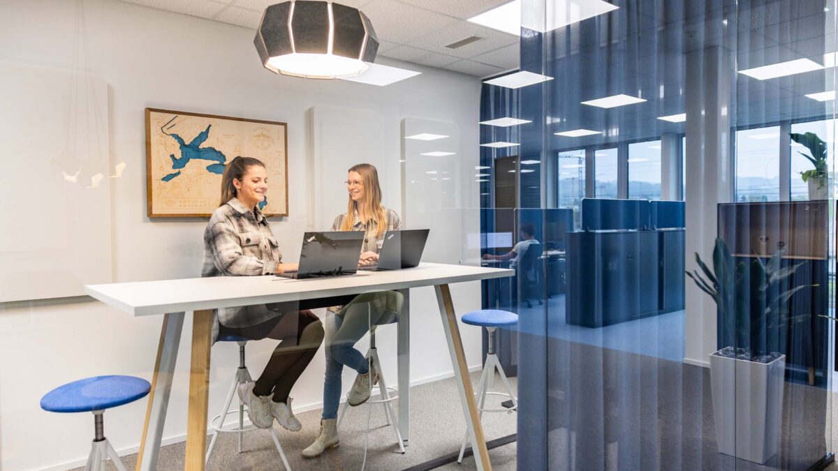 Zwei Mitarbeitende der Voicepoint AG sitzen mit Laptops an einem hohen Tisch und tauschen sich aus.