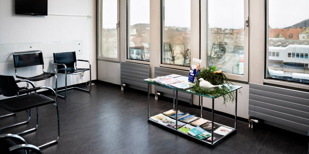 Salle d'attente d'un cabinet médical équipée d'une petite table et de chaises en cuir noir.