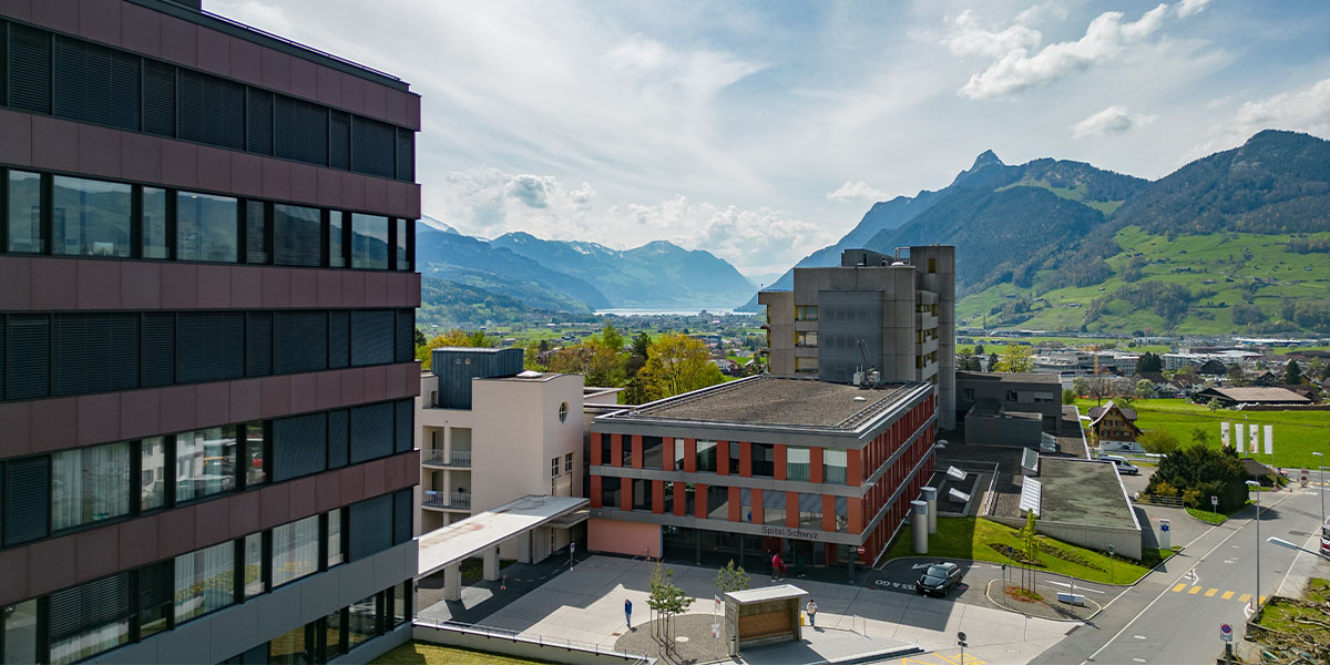 Luftaufnahme des Spitals Schwyz. Im Hintergrund sieht man die Schweizer Alpen.