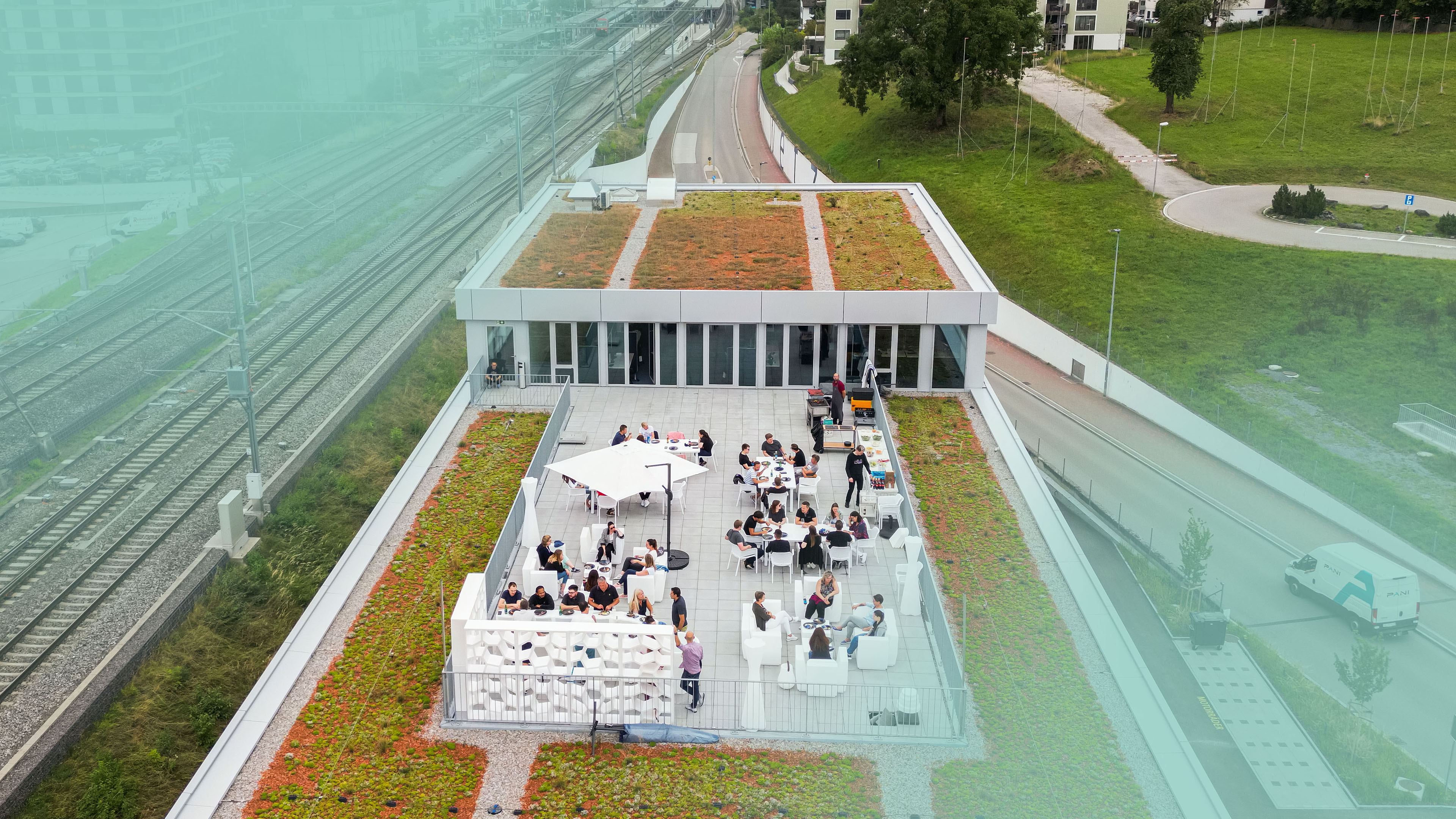 Mitarbeitende der Voicepoint AG sitzen und stehen auf der Dachterrasse am Standort in Wetzikon. Am Bildrand sind türkise Farbverläufe sichtbar.