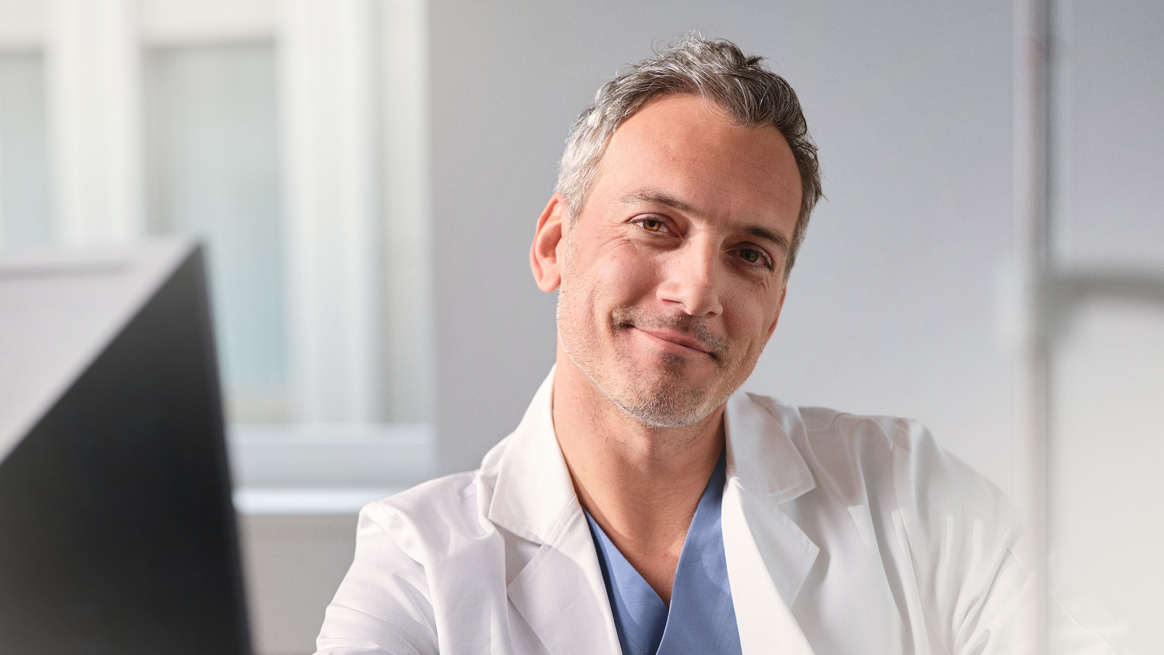 A doctor in a white coat smiles warmly at the camera.