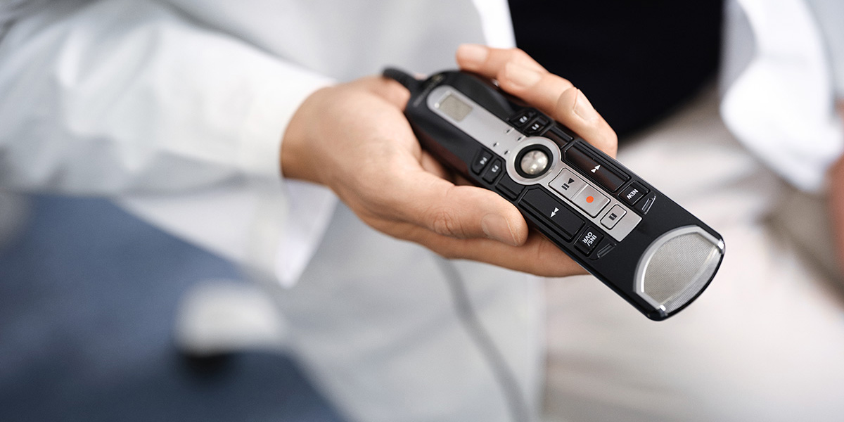 Ein Arzt im weissen Kittel hält ein OM SYSTEM RecMic 4010 Diktiergerät in der Hand