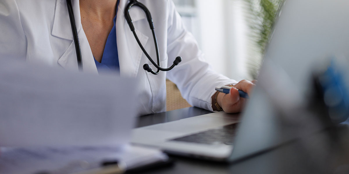 A doctor sits at a desk and documents a patient consultation.