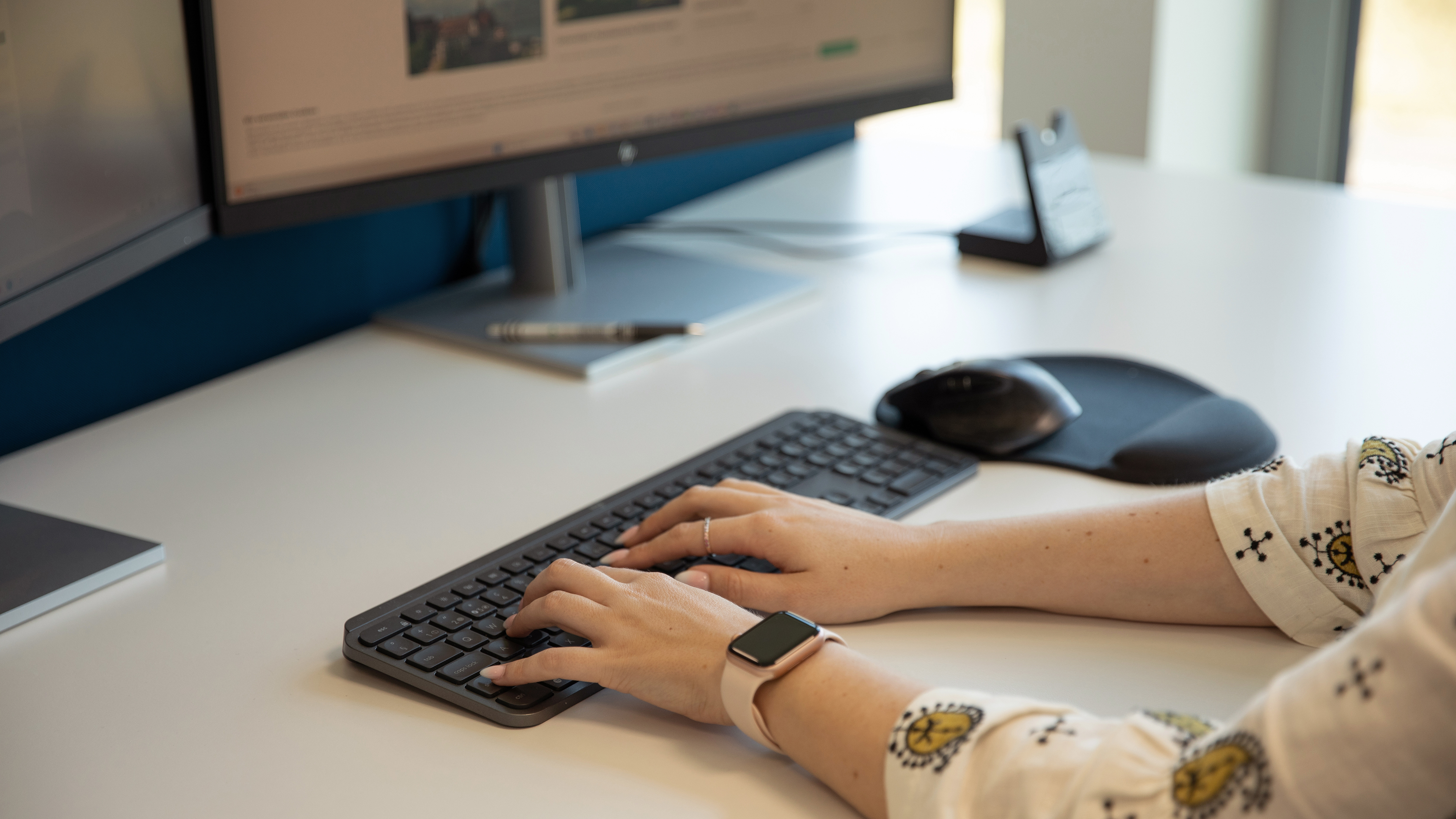 Employee sitting at a desk, working with two screens and typing on the keyboard.