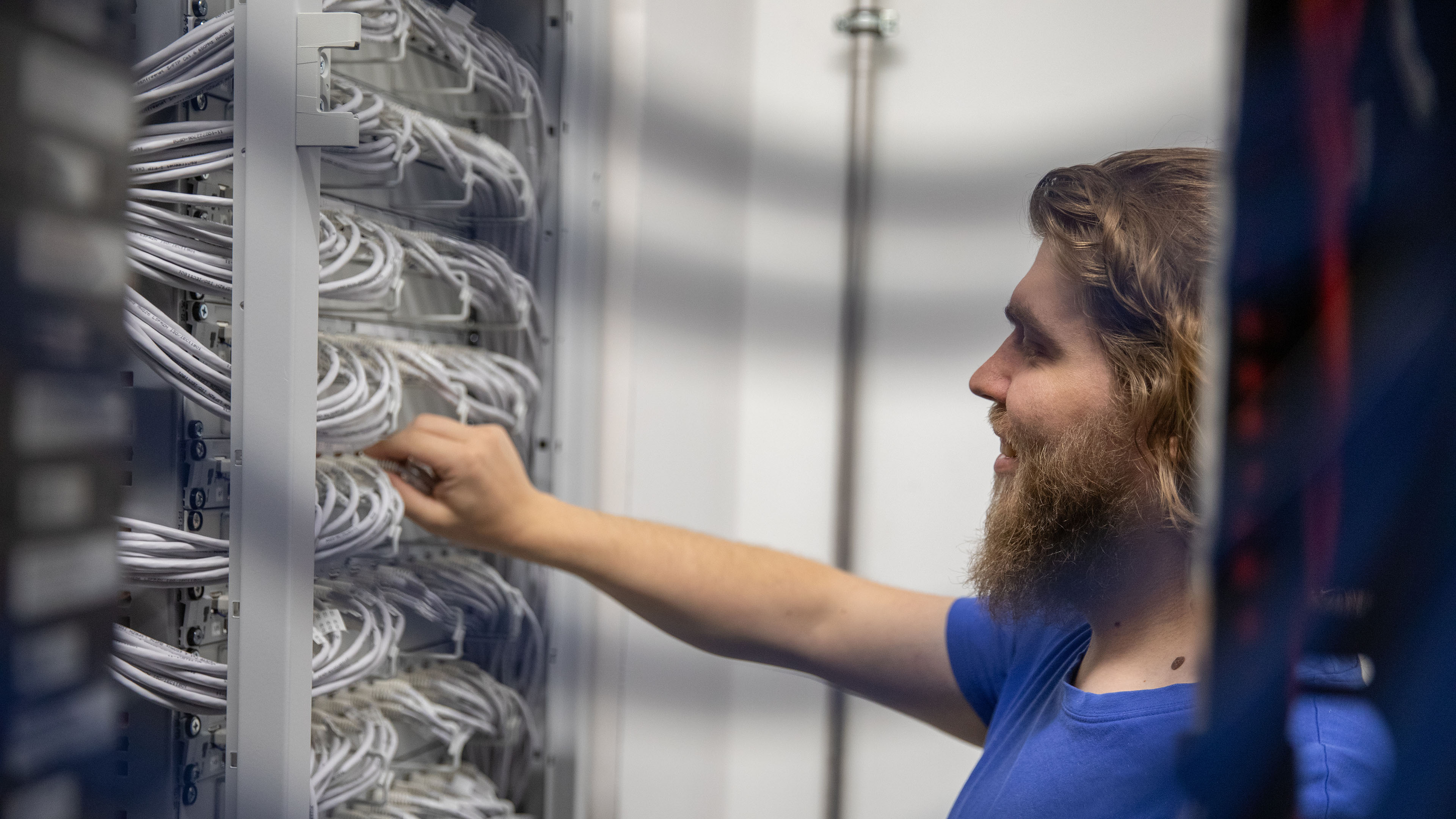 Voicepoint AG employee checks cable connections on the Ethernet patch panel in the technical room.