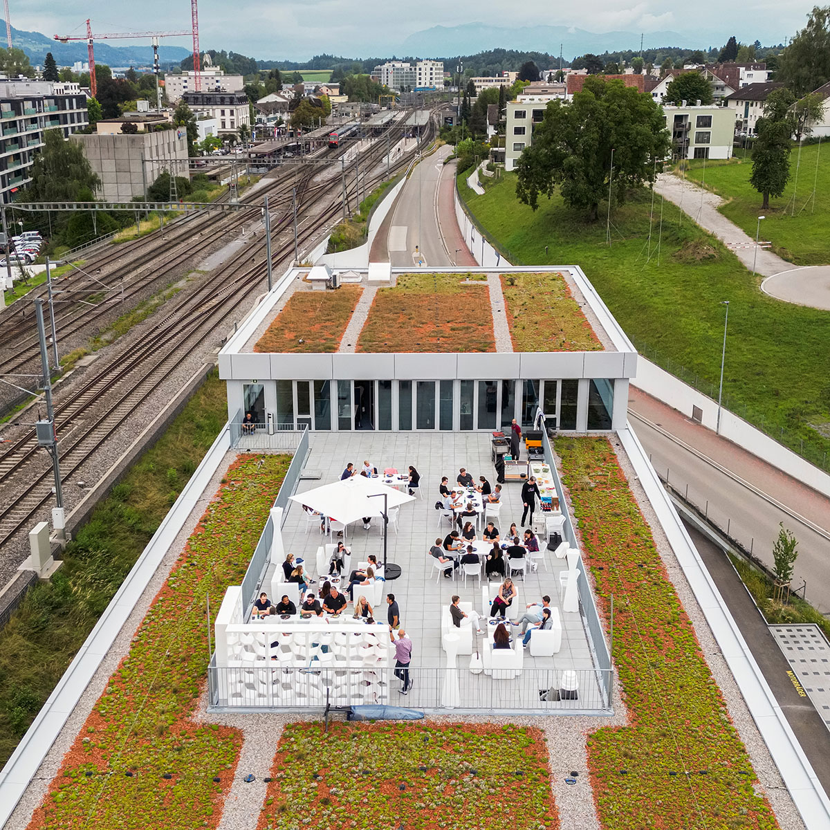 Mitarbeitende der Voicepoint AG sitzen und stehen auf der Dachterrasse am Standort in Wetzikon und nehmen an einem Apéro teil.