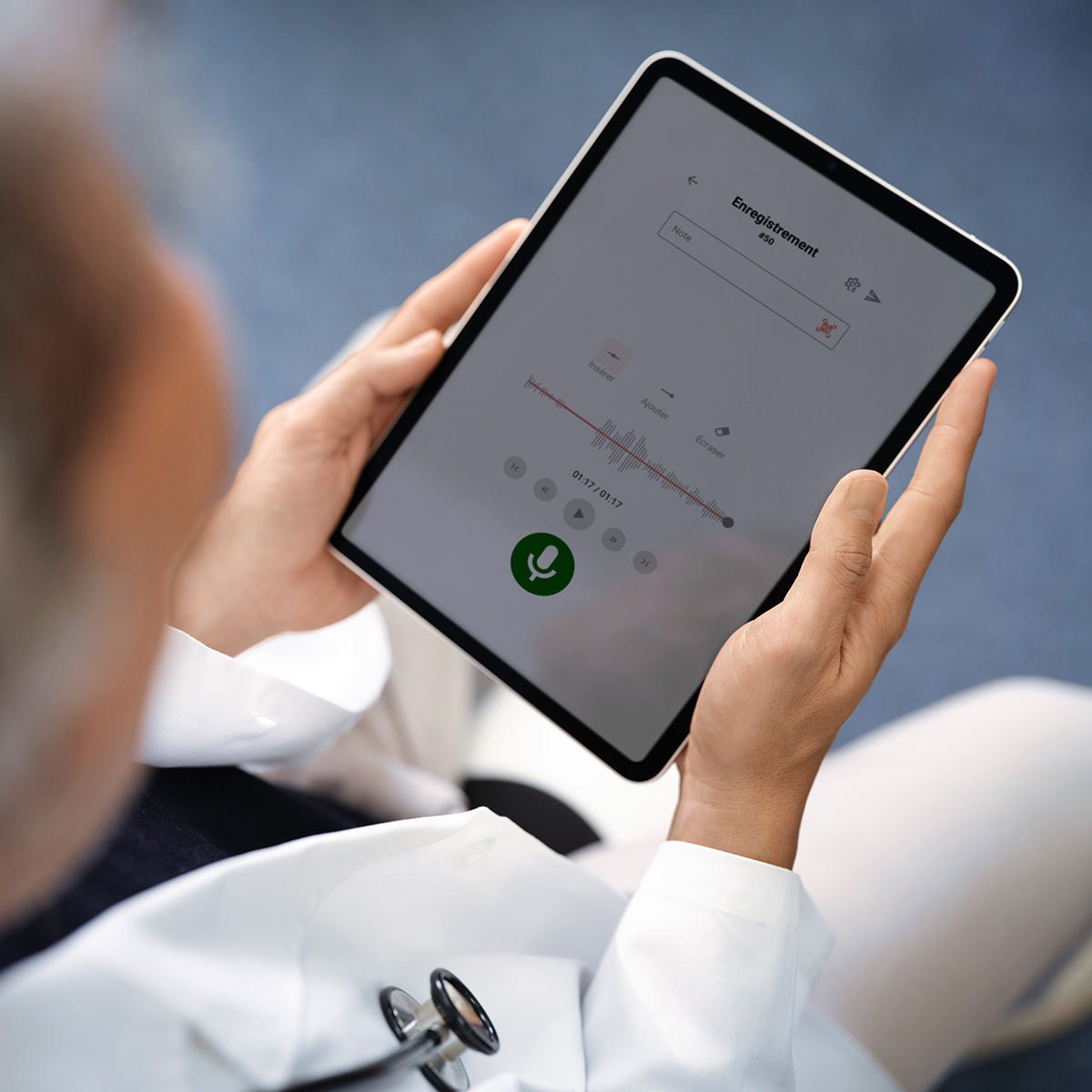 Une personne en blouse blanche tient dans ses mains une tablette sur laquelle apparaît l'interface utilisateur de Voicepoint Xenon.