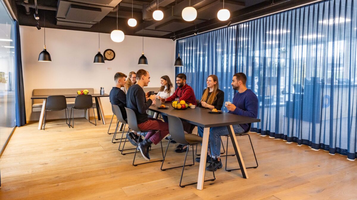 Mehrere Mitarbeitende der Voicepoint AG sitzen in der Cafeteria an einem langen Tisch und unterhalten sich.