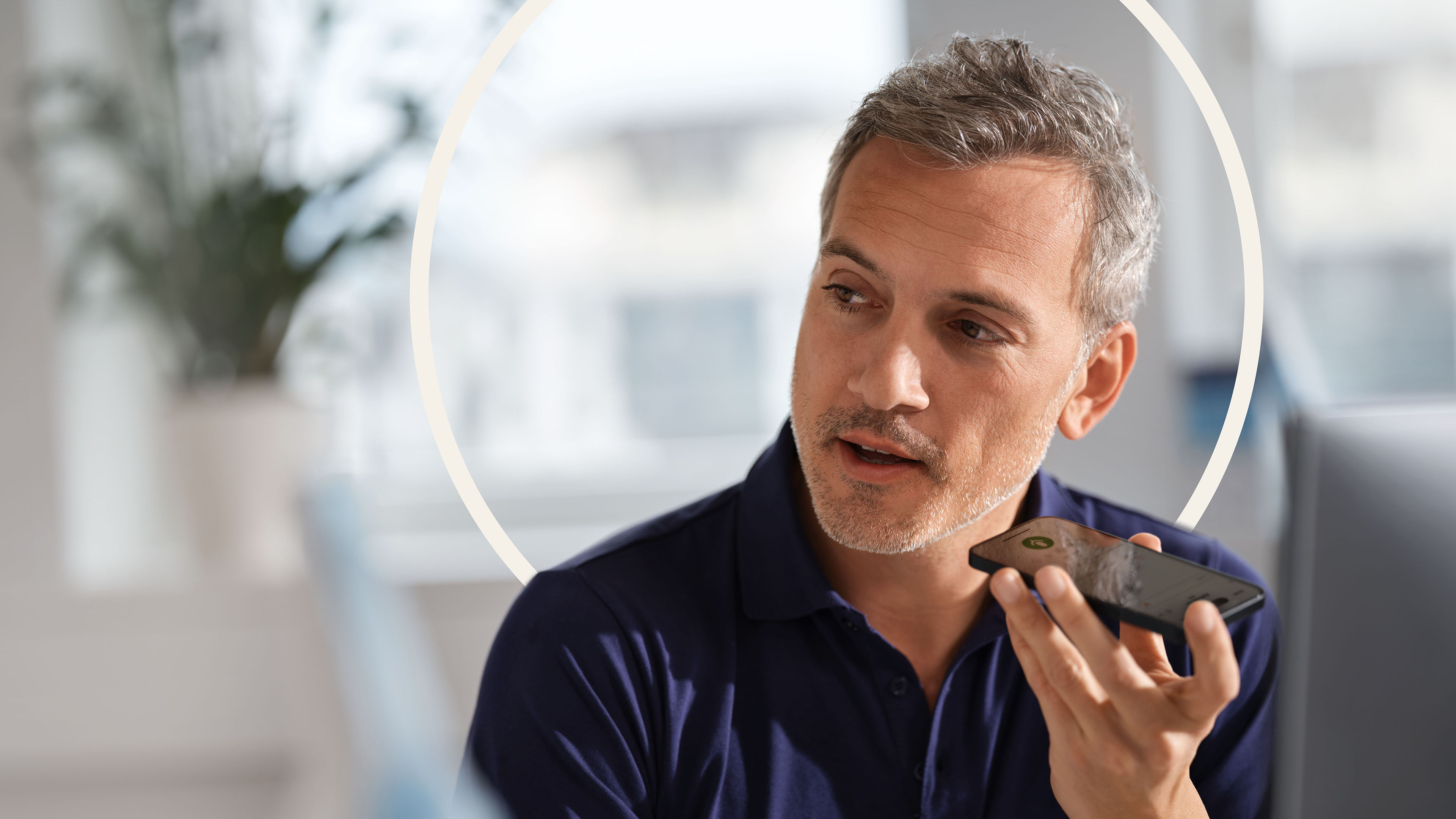 Arzt im blauen Poloshirt diktiert am Arbeitsplatz mit einem Smartphone