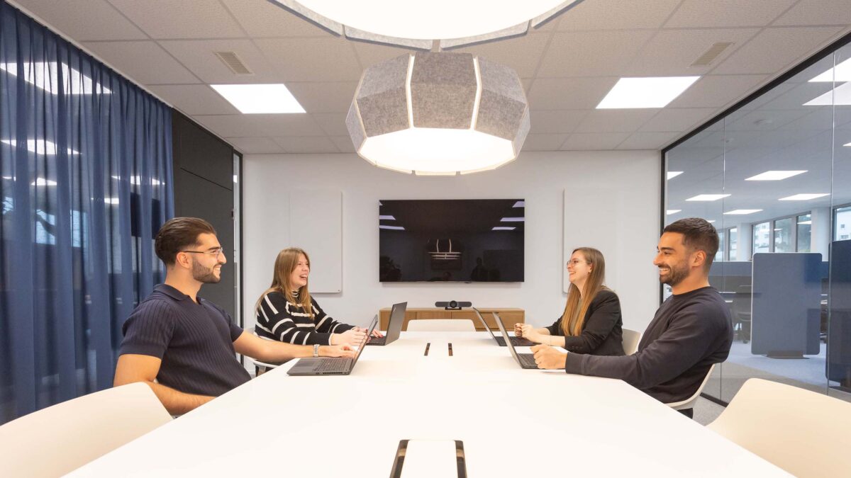 Vier Mitarbeitende der Voicepoint AG sitzen sich im Sitzungszimmer an einem langen Tisch gegenüber und arbeiten an ihren Laptops.