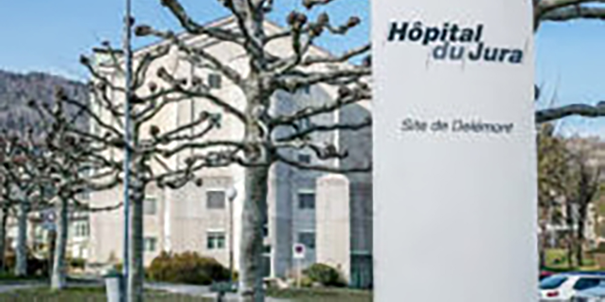 Gebäude des Hôpital du Jura, Standort Delémont, mit Eingangsbereich und sichtbarem Spitalschild im Vordergrund.