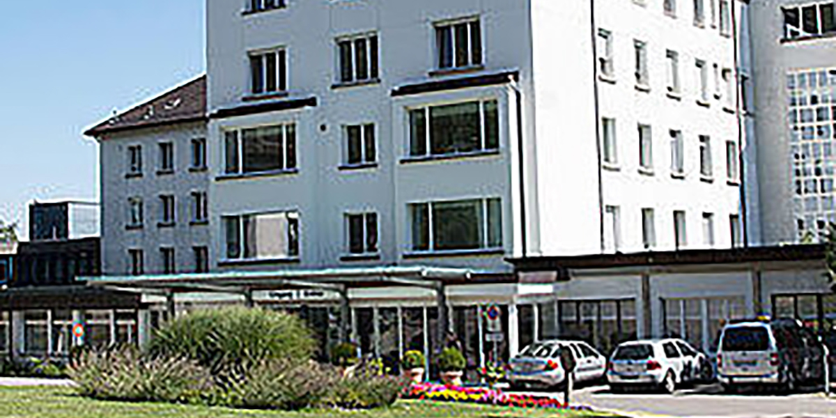 Frontansicht des Spitalzentrums Biel mit mehrstöckigem Gebäude, Eingangsbereich und parkenden Fahrzeugen.
