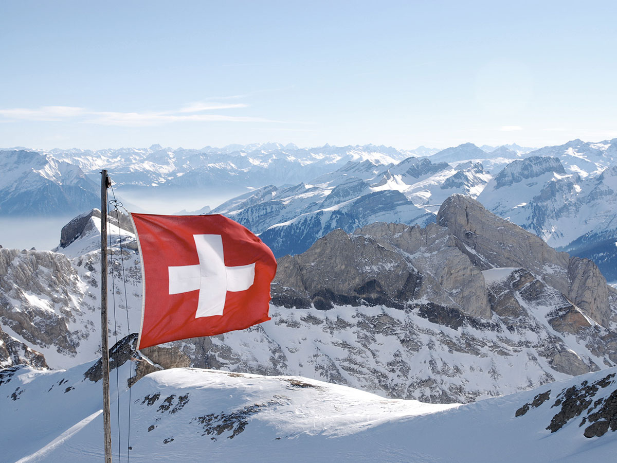 Drapeau suisse sur un sommet enneigé avec panorama alpin, image symbolique du cloud Voicepoint exploité en Suisse.