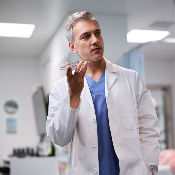 Un médecin en blouse blanche se tient dans un couloir, un smartphone à la main, et dicte avec Voicepoint Xenon.