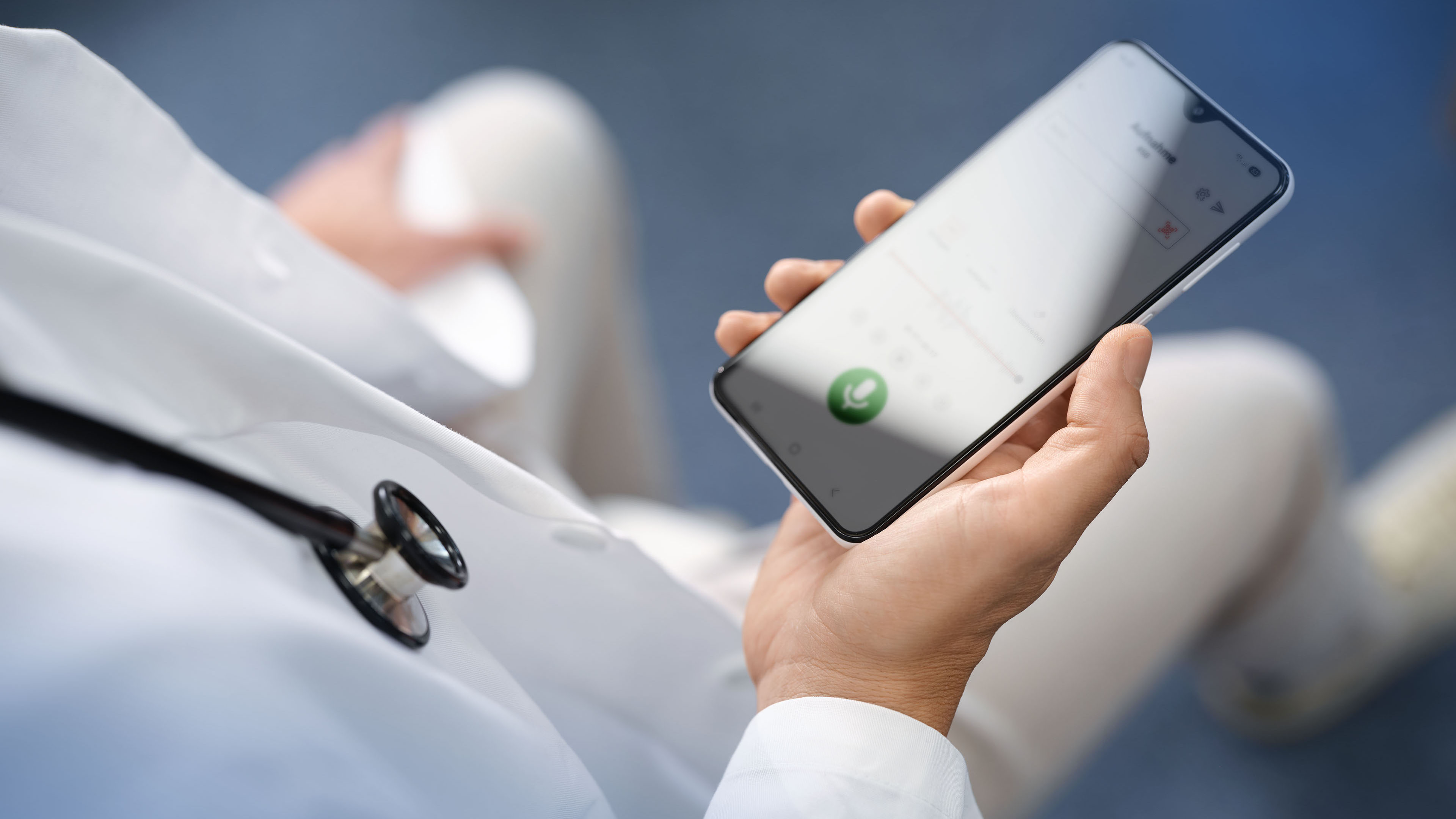 Arzt im weissen Kittel sitzt und startet auf dem Smartphone in seiner Hand eine Diktataufnahme mit der Voicepoint Xenon App.