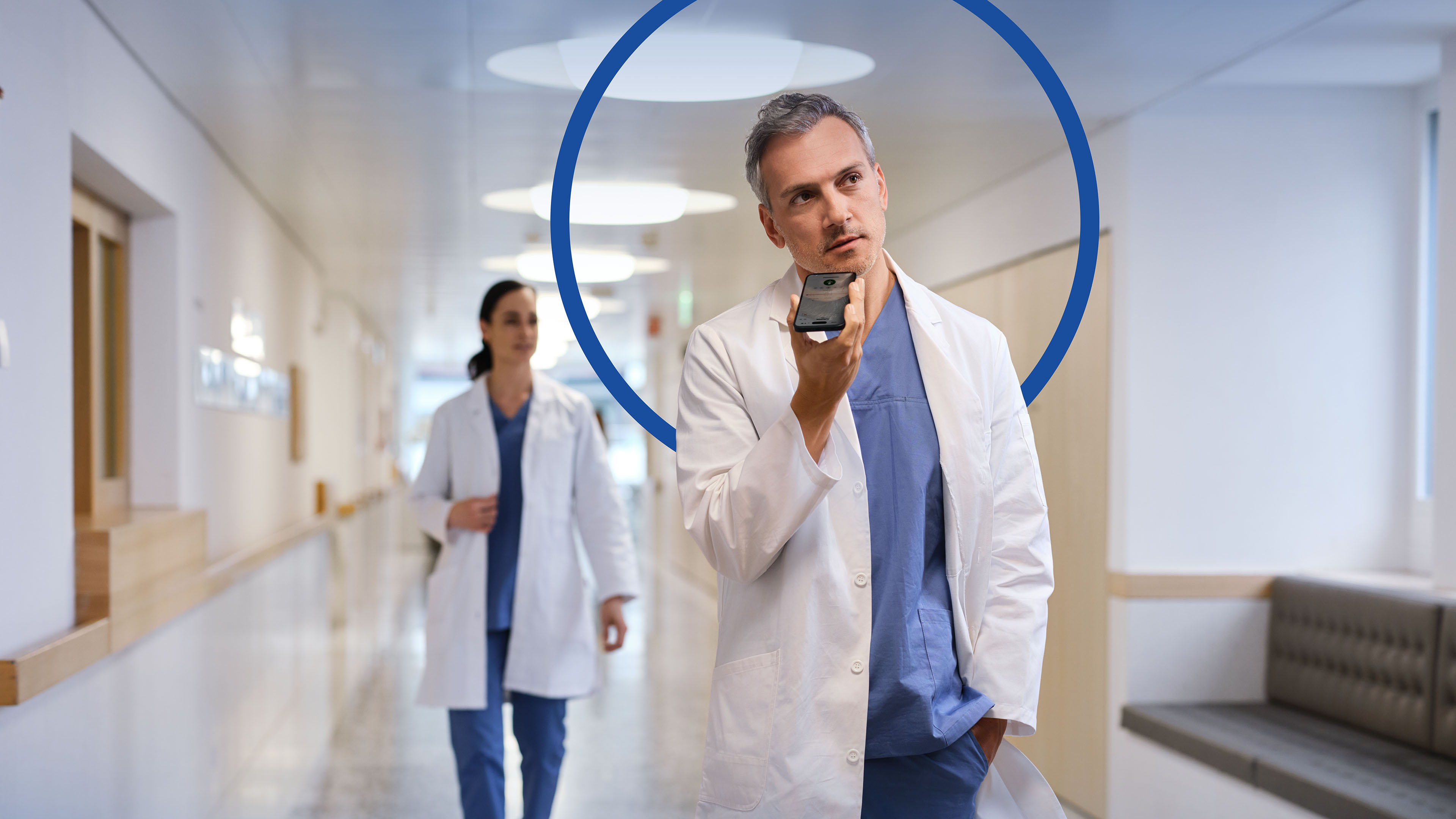 Arzt läuft durch den Klinikflur und diktiert mit dem Smartphone. Im Hintergrund zeigt sich ein blauer Kreis als Gestaltungselement.